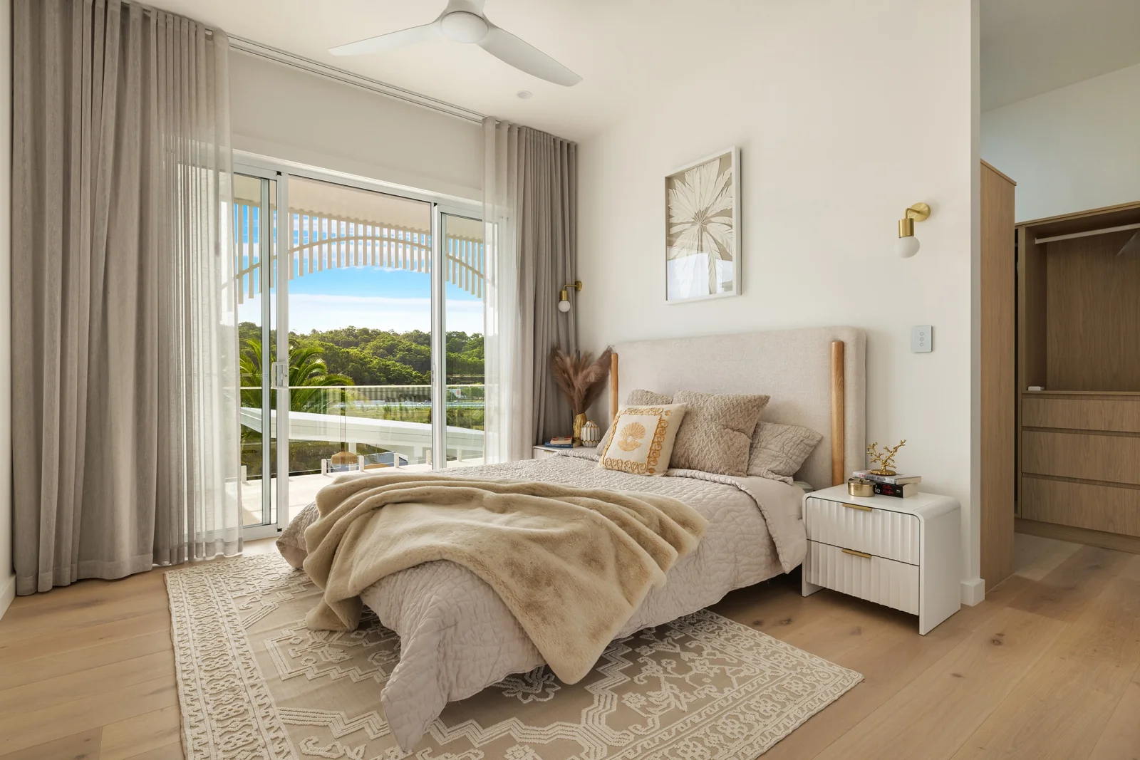 A light-filled bedroom with a neutral upholstered bed and garden outlook
